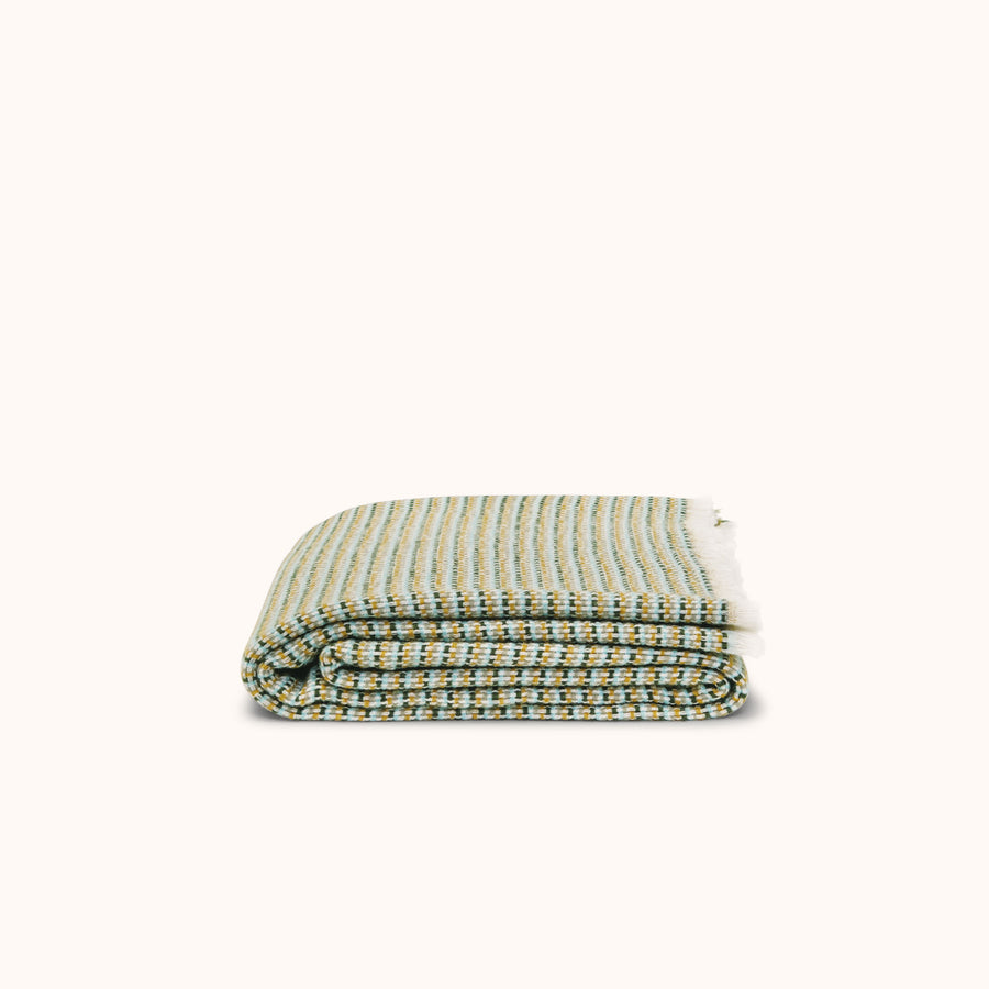 A folded wool/cotton blend blanket with a subtle woven stripe pattern in golden yellow, blue, and green hues.