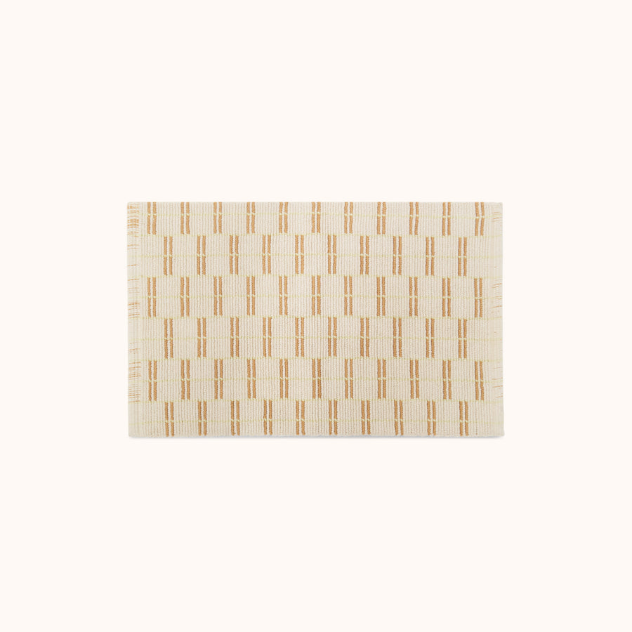 A rectangular bathmat featuring a geometric pattern in lime, tan, and natural colors.