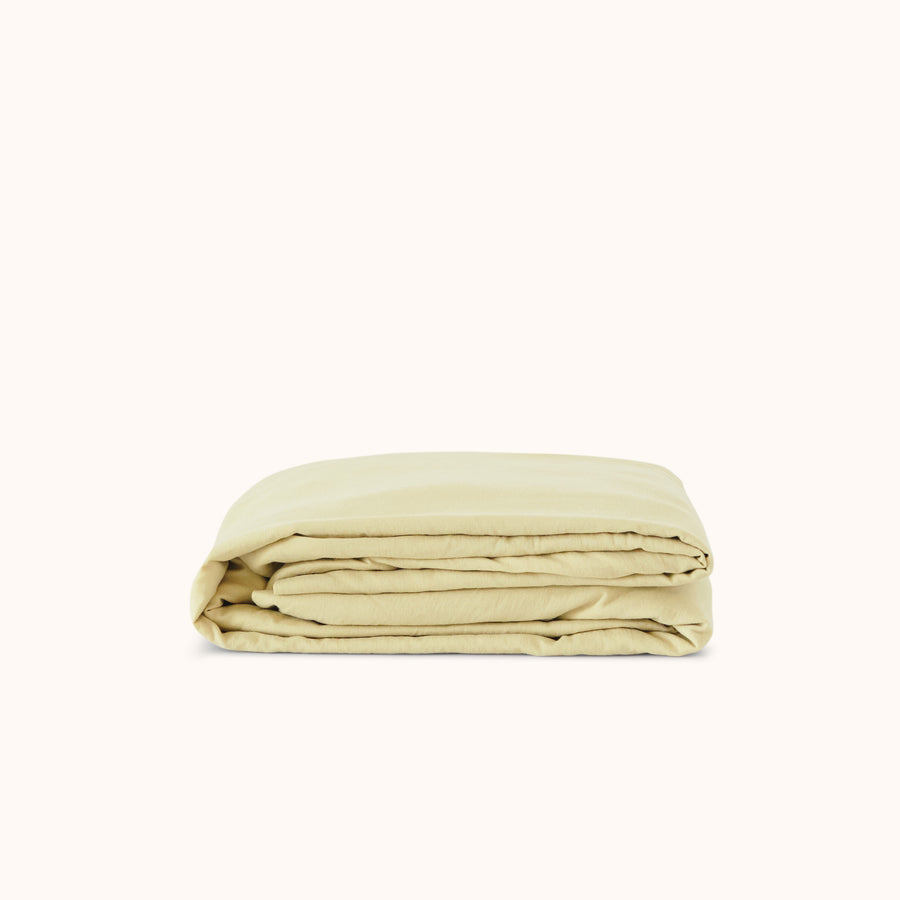 A folded Límon / light yellow fitted sheet made of organic cotton, displayed on a neutral background.
