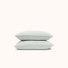 A set of two Mist / light blue pillowcases made from organic matte sateen, displayed neatly stacked on top of each other against a white background.