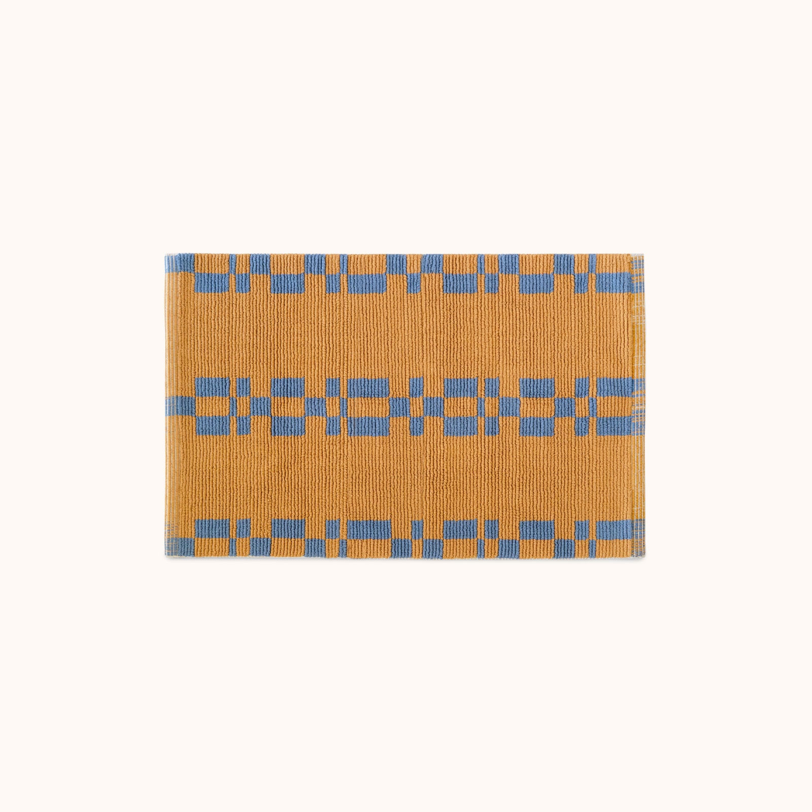 A rectangular, hand looped bathmat with a geometric pattern featuring blue and camel colors.