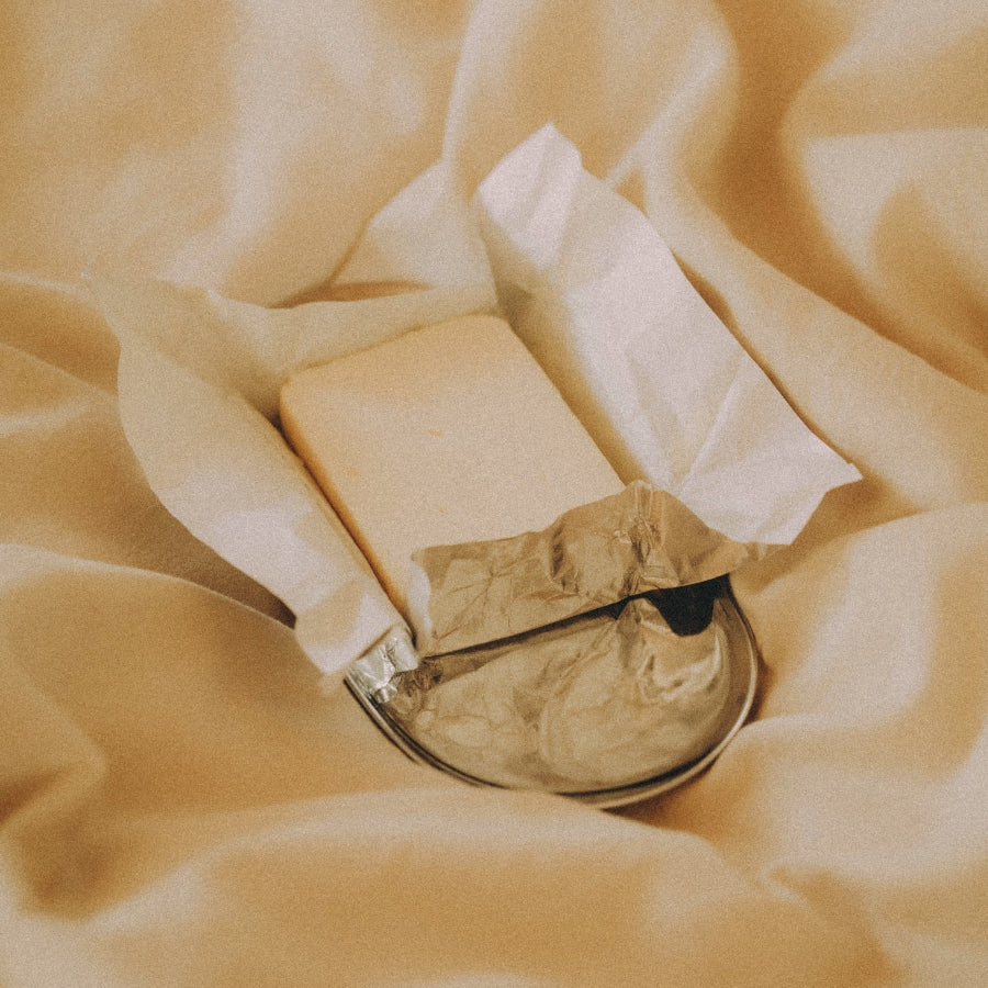 A small rectangular pad of butter wrapped in silver foil on top of a silver tray, set on draped yellow fabric.