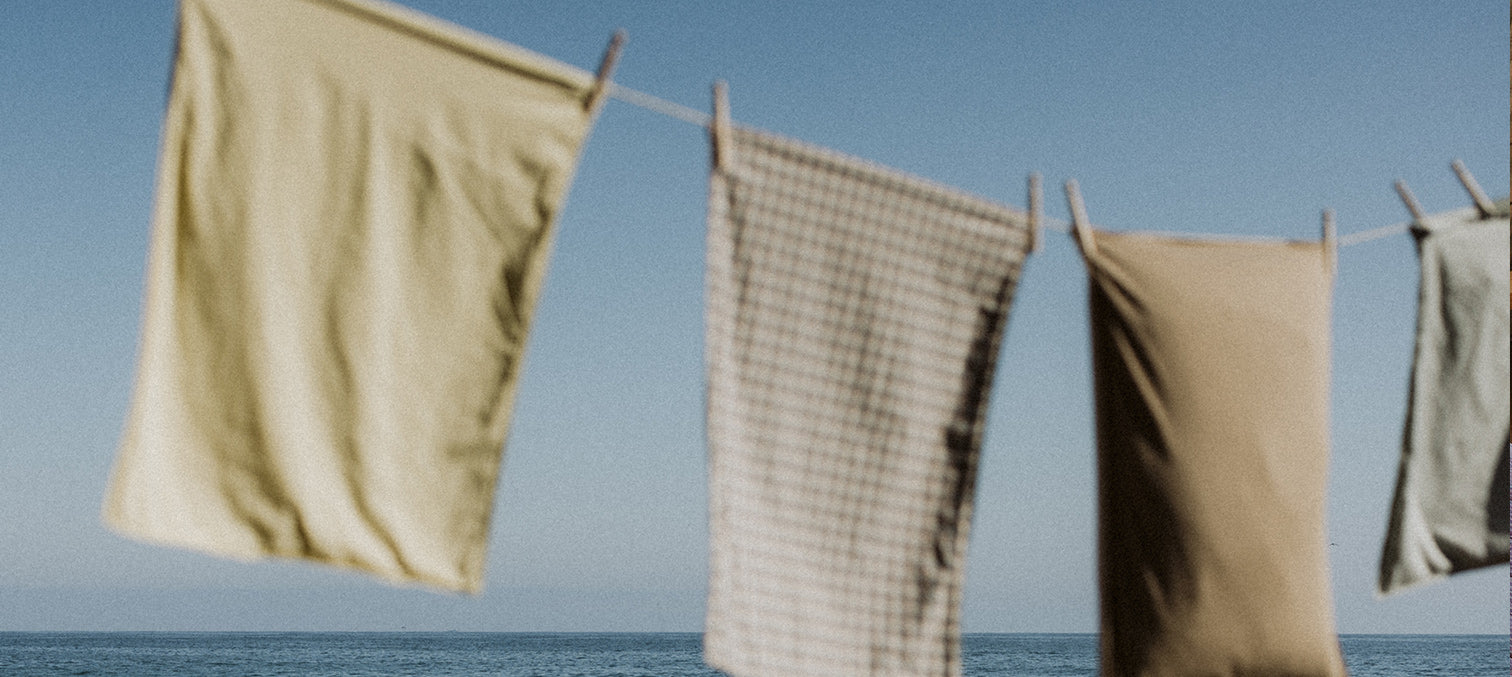 Three pillowcases hanging on a clothes line with a clear blue sky and water in the background