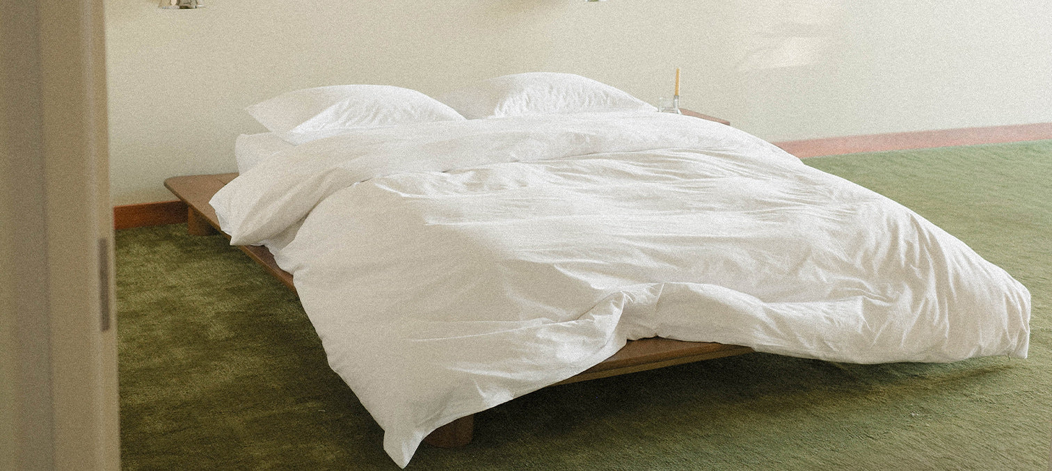 Bed with white comforter in a room with green carpet and beige walls