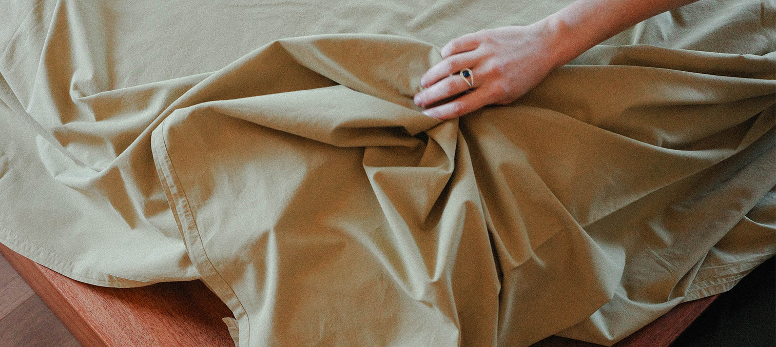 Person holding beige fabric with a hand wearing a ring.
