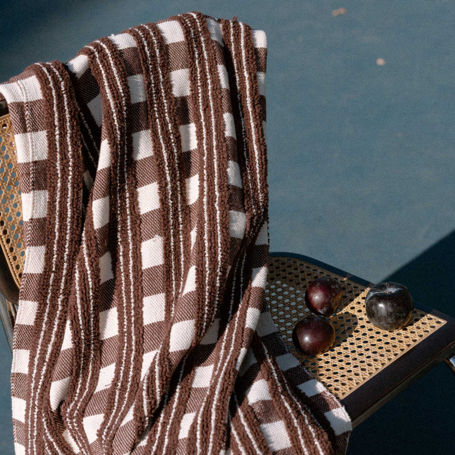 Brown and natural checkered blanket draped over a wicker chair with a blurred background