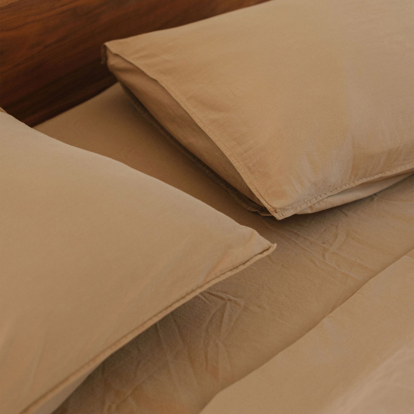 A close up of the top of a bed and two beige pillows against beige sheets 