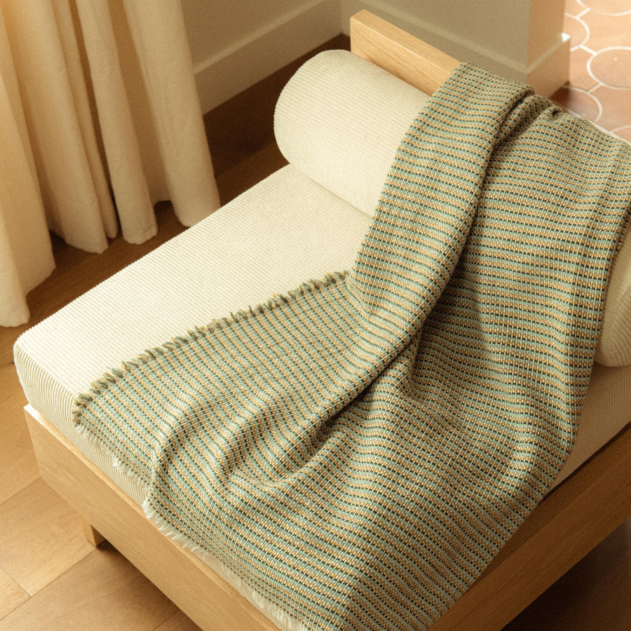  A blanket with a woven stripe pattern in golden yellow, blue, and green hues draped over a chair.