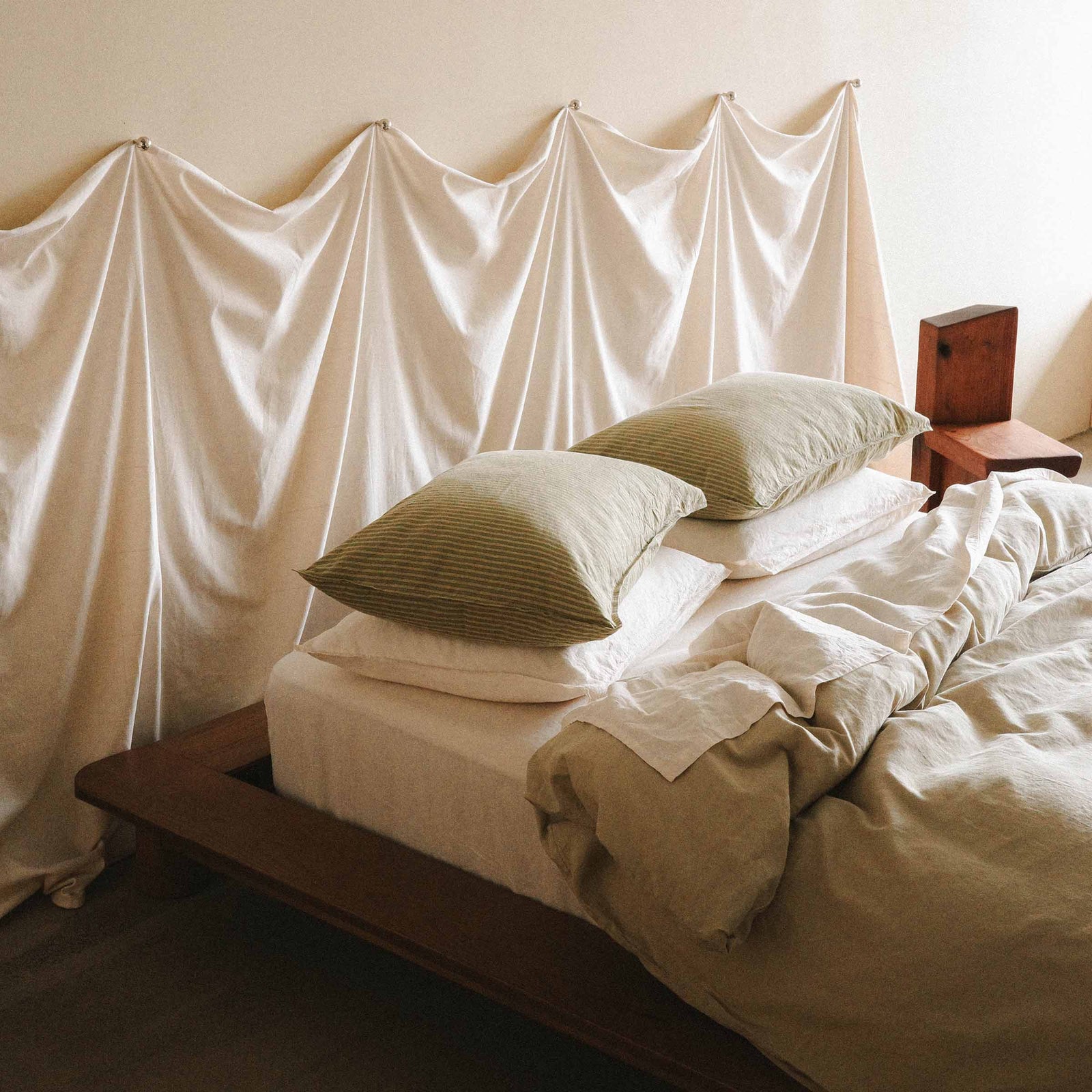A platform bed with green and cream sheets and four pillows, two cream and two green stripes