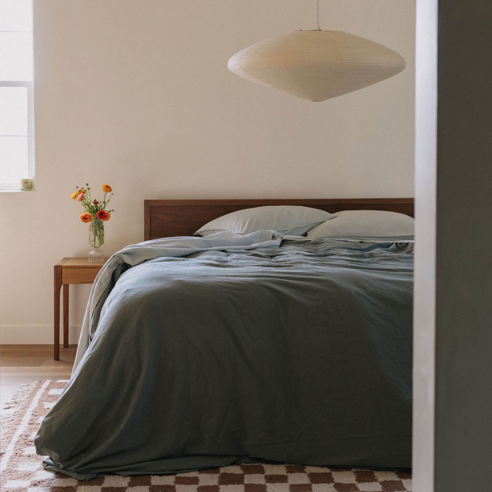 A bed dressed with mist / light blue sheets and pillowcases and a green duvet cover ina  bedroom setting. 