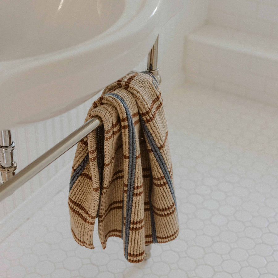 A bath mat with brown and blue stripes hung over a bar on the underside of a bathroom sink.