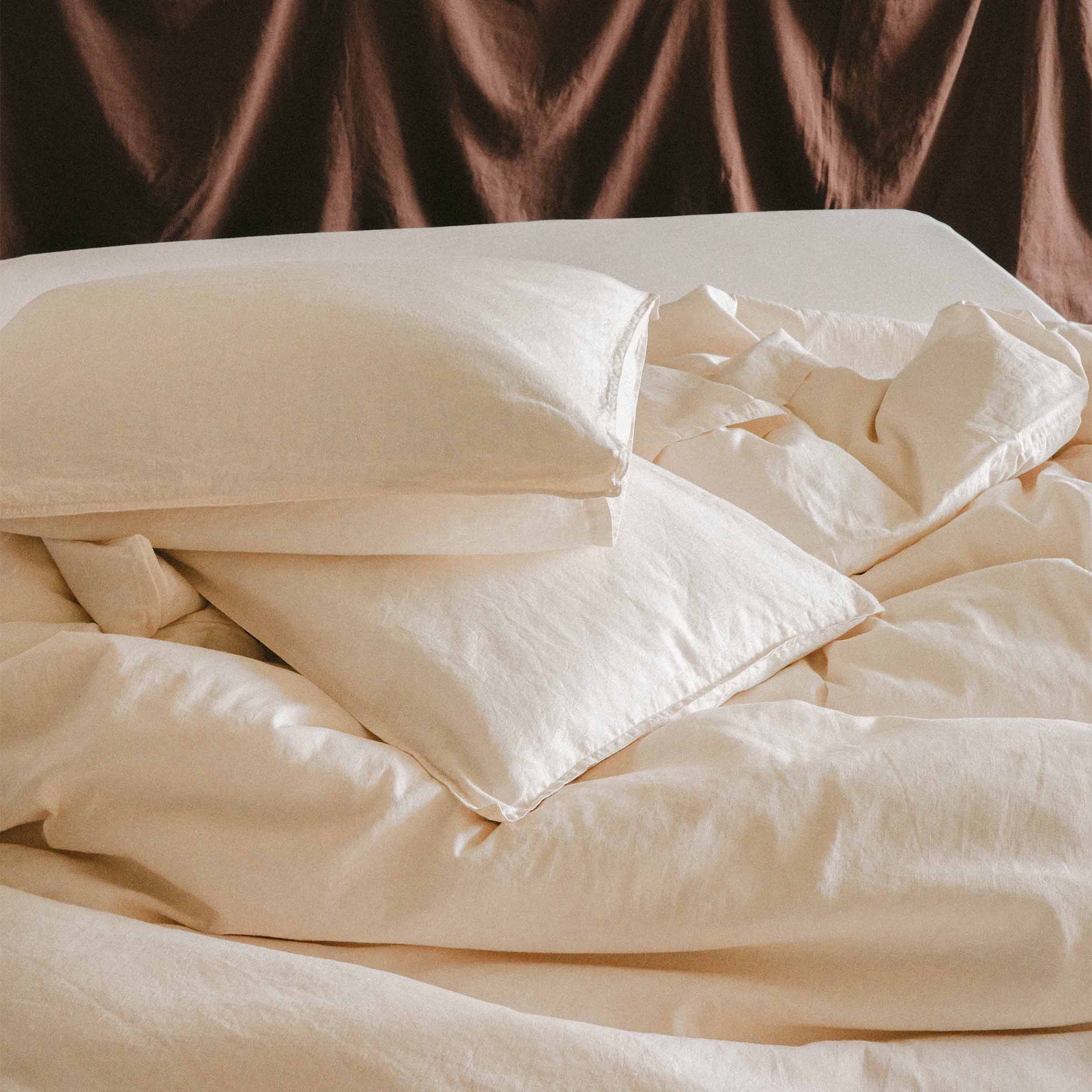 Close up of unmade bed with two pillows and a duvet cover in cream / white