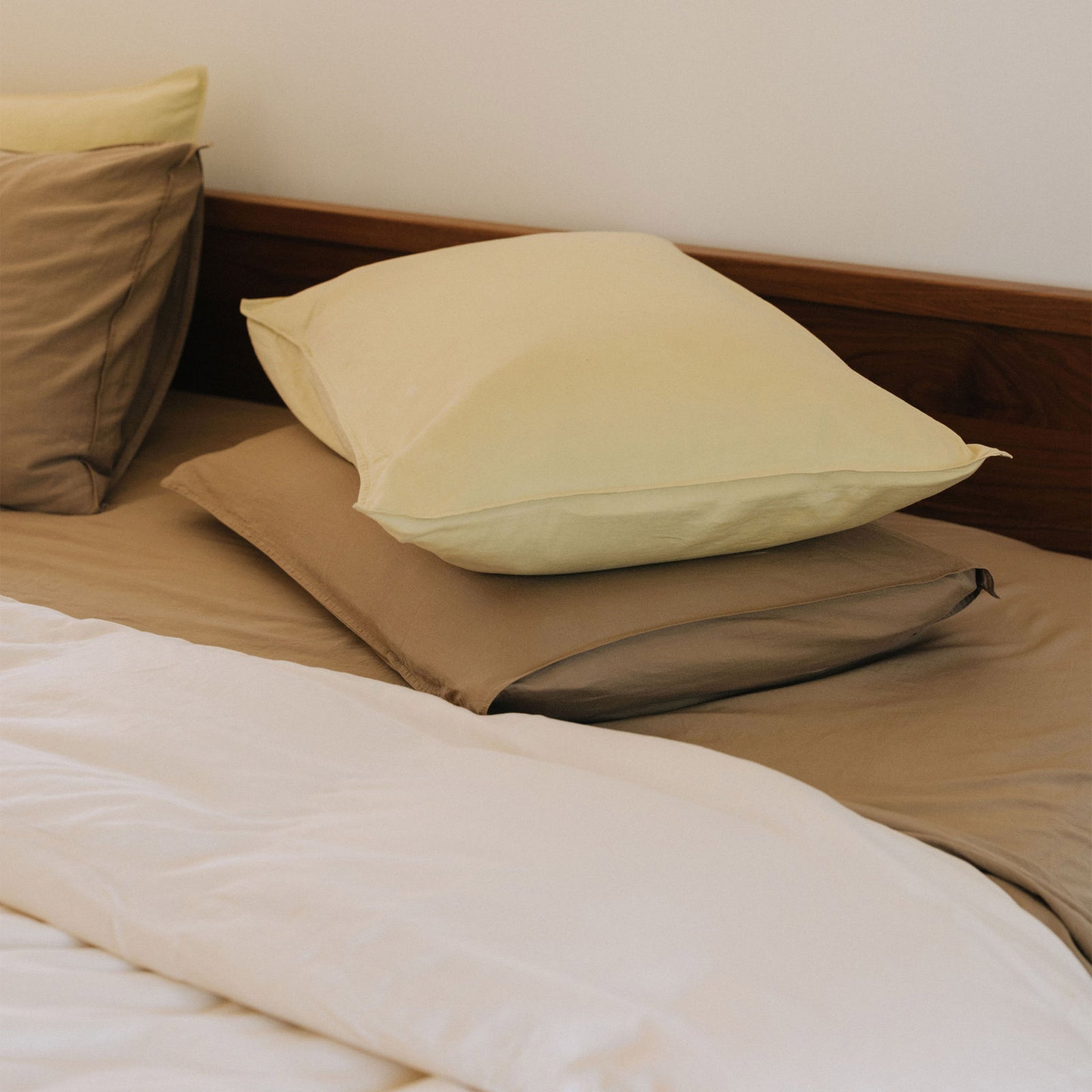 A stack of pillows, beige beneath and lime on top. The pillows are on a bed with beige and white sheets