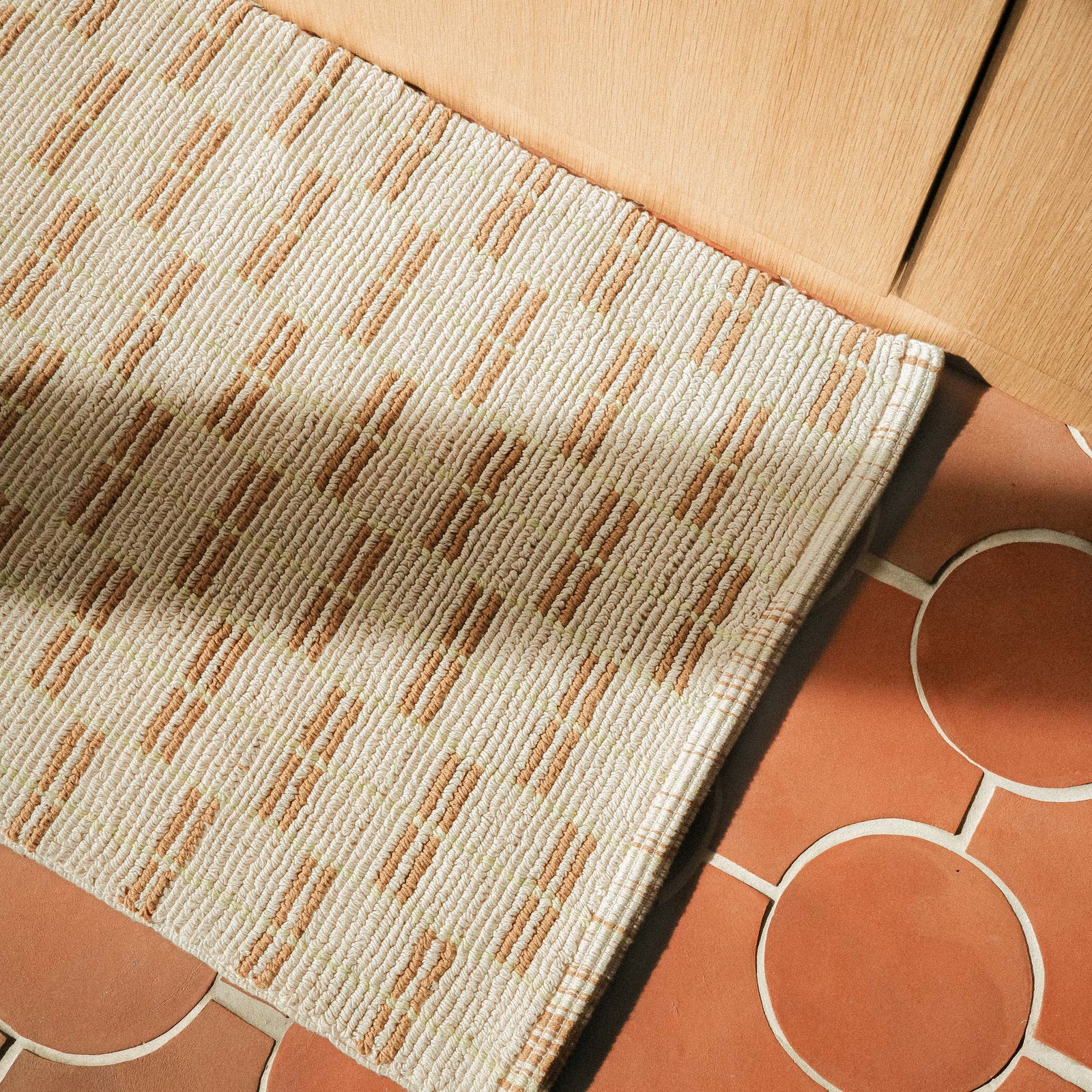 Close up of a tan bathmat featuring a brown and lime geometric pattern on a tile floor.