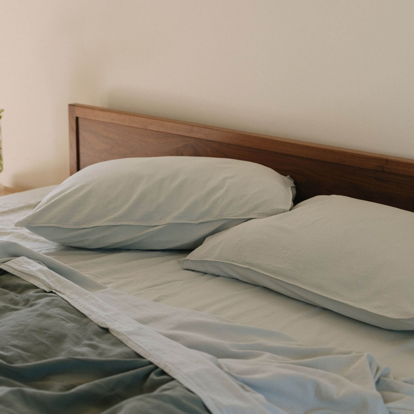 A bed with pale blue / Mist sheets and pillowcases shown with a deeper green duvet cover against a dark brown headboard