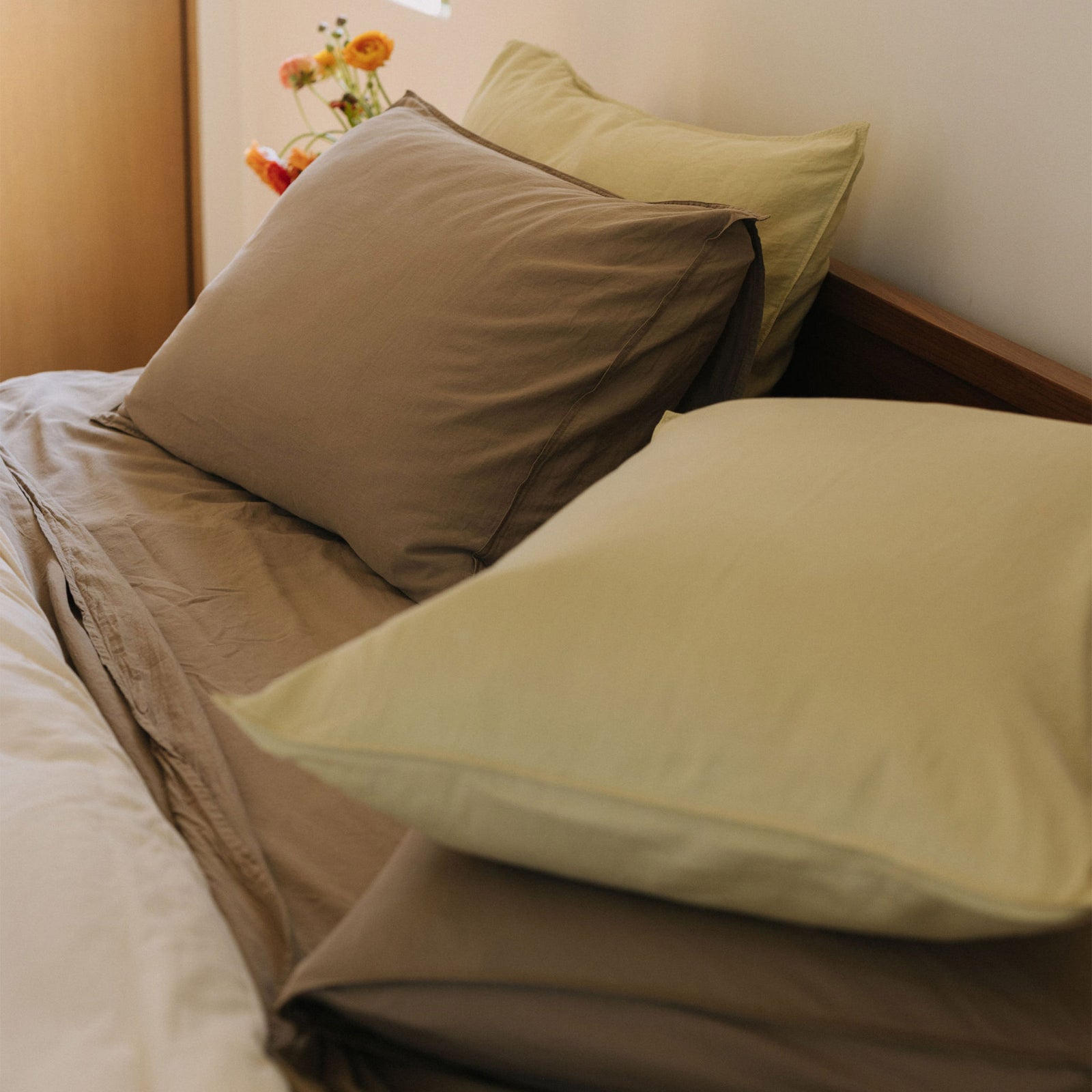 The top half of a bed with lime and beige colored pillows over a white and beige sheets