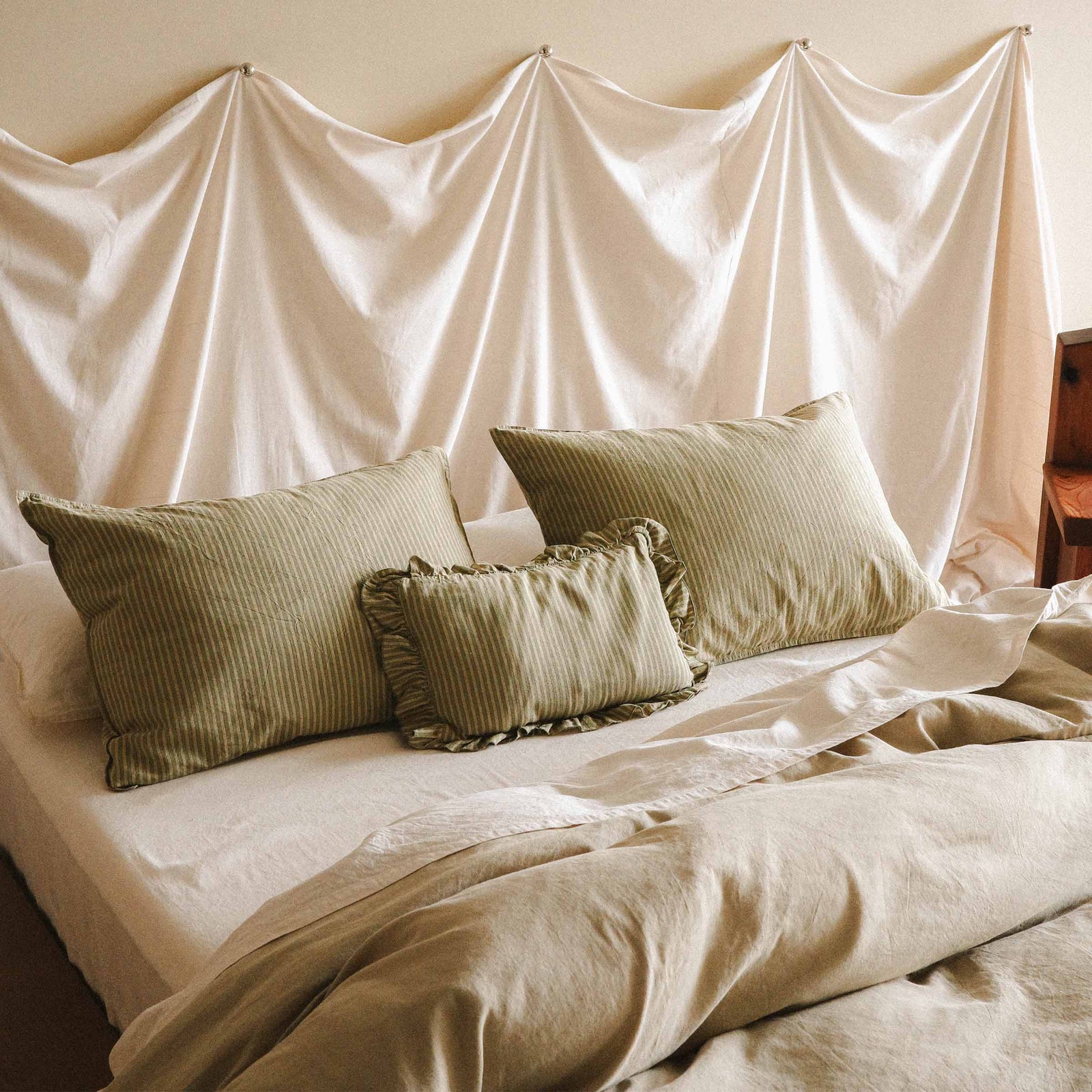 Bed with green striped pillows and cream sheets and a green duvet cover in a bedroom setting