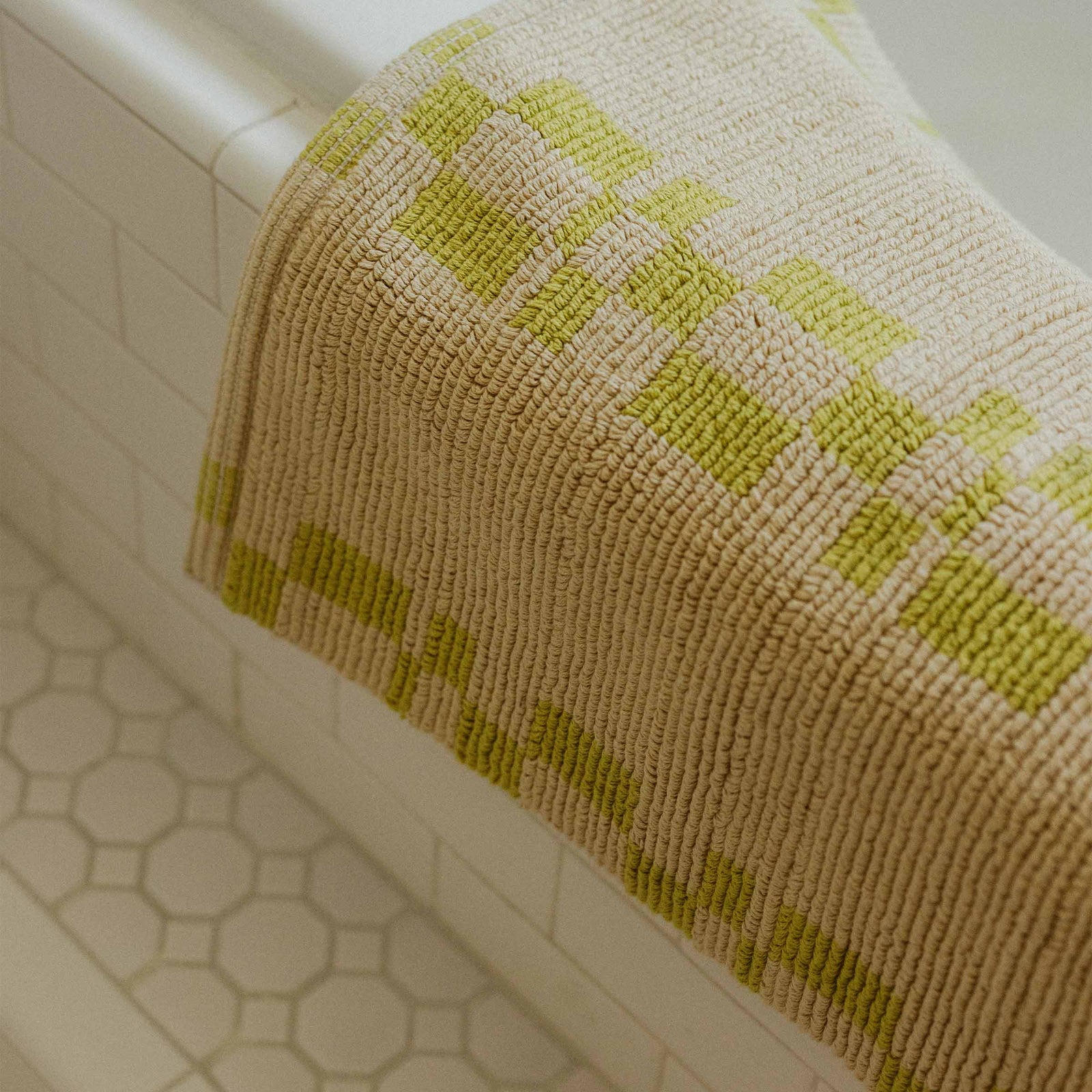 A bathmat with a lime geometric pattern and a beige background draped over a tile tub.