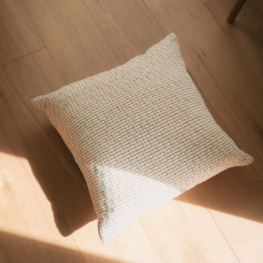 A throw pillow with a beige and brown hazelnut stripe texture on a wooden floor.