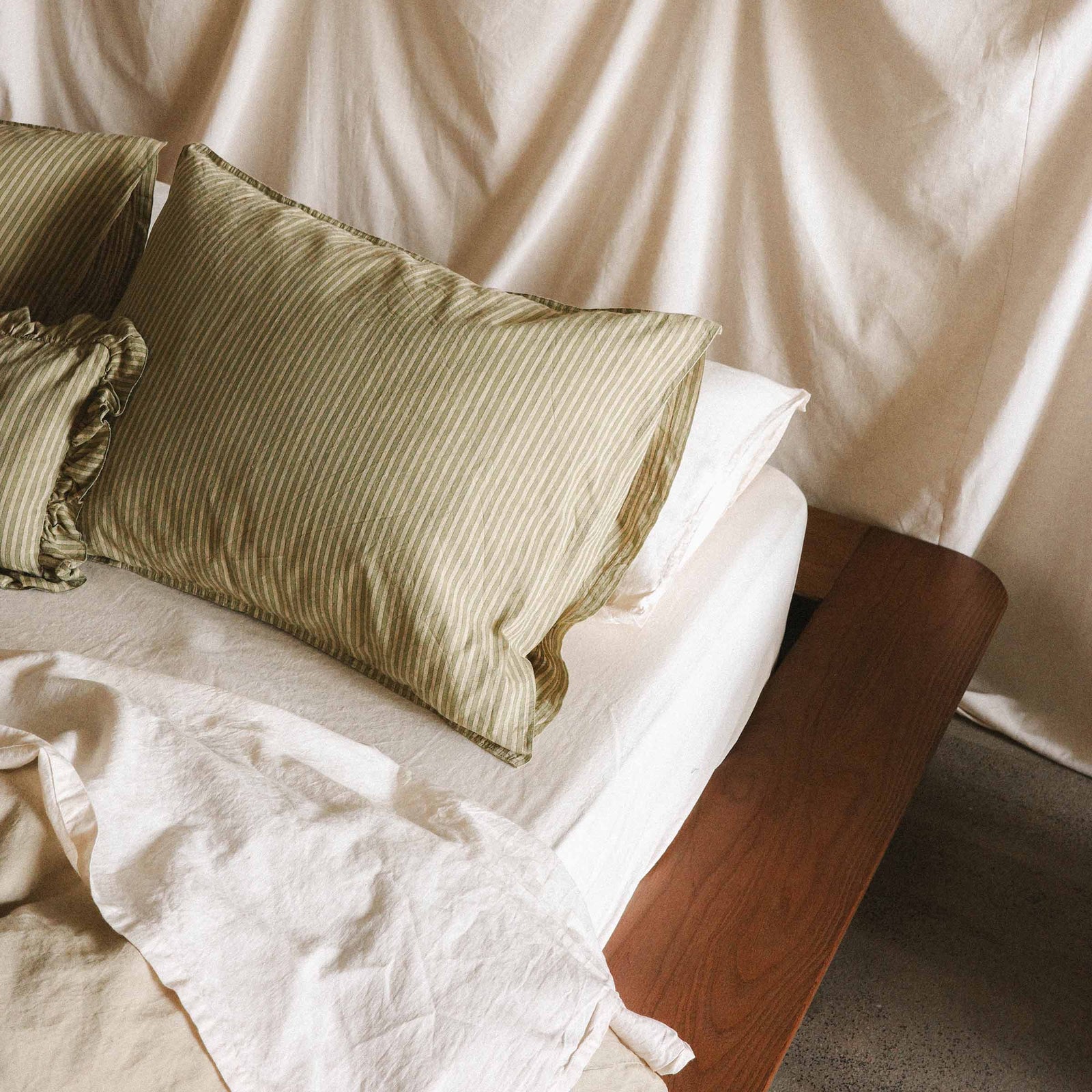 Close up of the corner of a bed with a green stripped pillowcase and cream / white sheets 