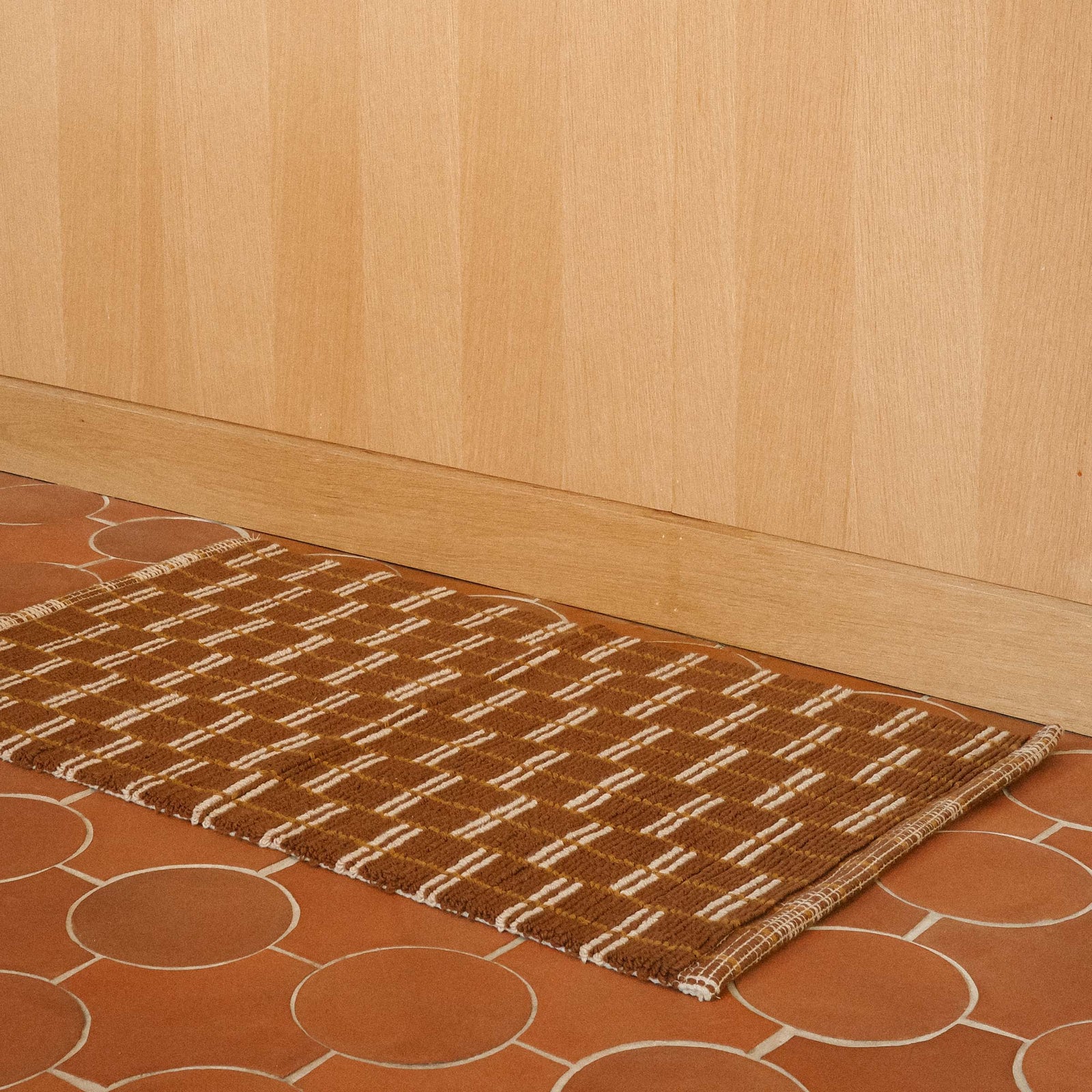 A brown bathmat constructed of tiny loops with a brown and tan geometric pattern.