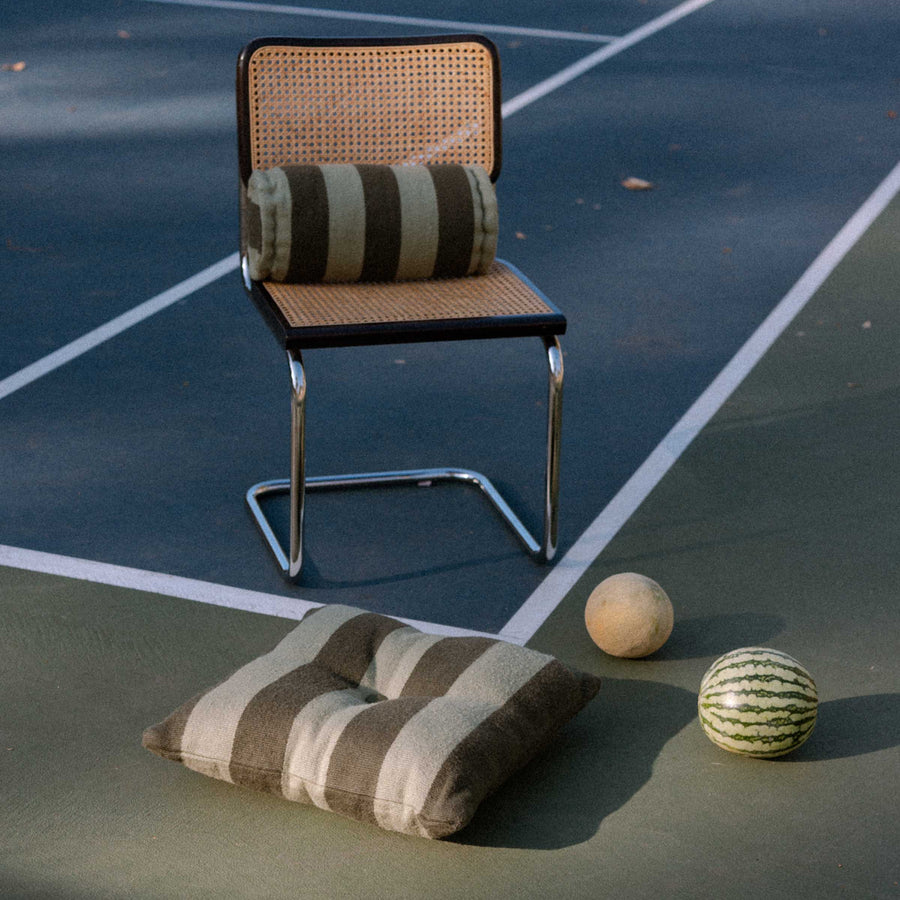 Chair with striped green pillow and bolster on a tennis court with two melons.