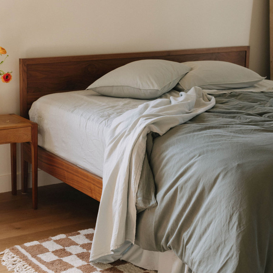 A bedroom setting with a bed dressed in Mist matte sateen sheets paired with a matte sateen pacific duvet cover