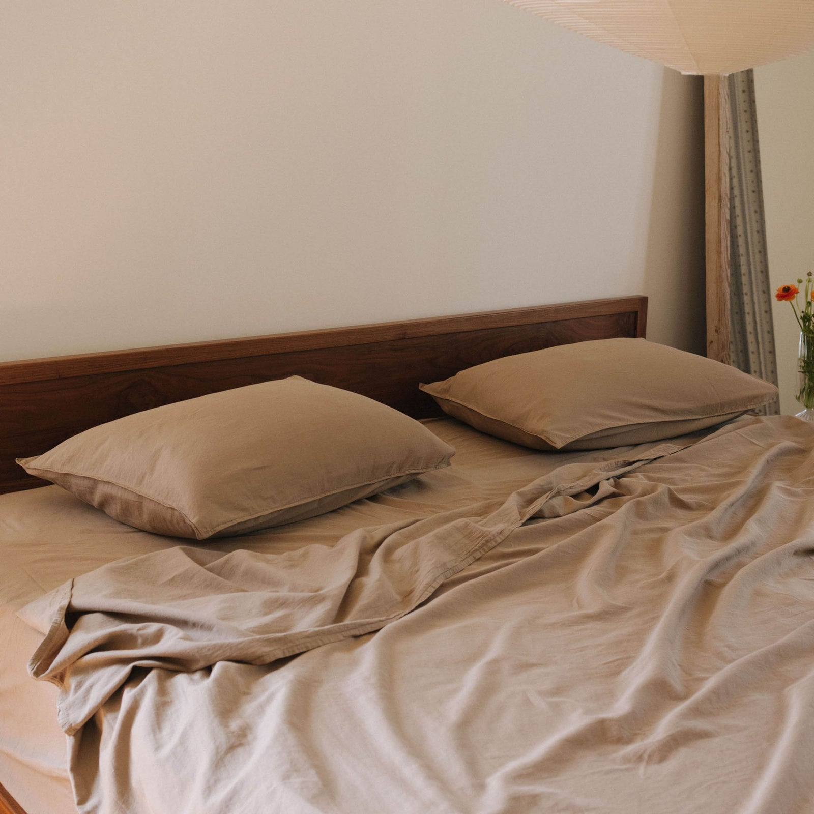 Close up on the top half of a bed dressed in Dune / brown sheets with a pendant paper lantern hanging over the bed. 
