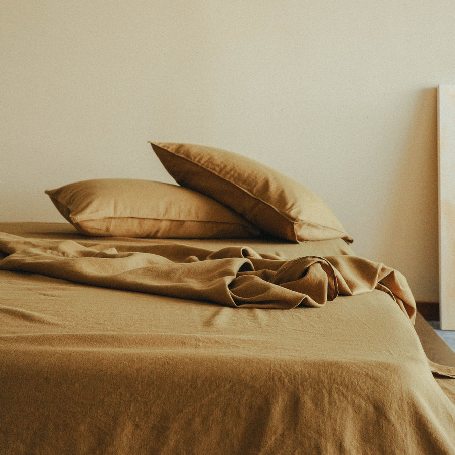 A brown bedspread and pillows on a bed against a beige wall.
