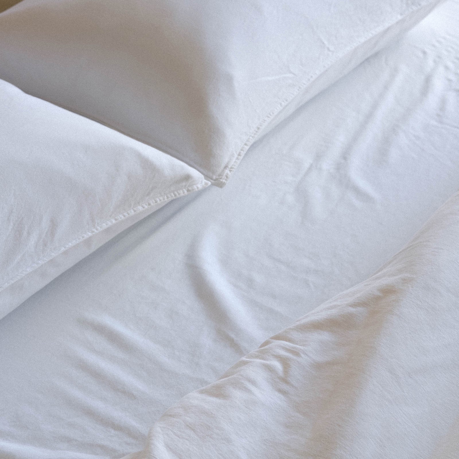 A close up of two white matte sateen pillows and white matte sateen sheets