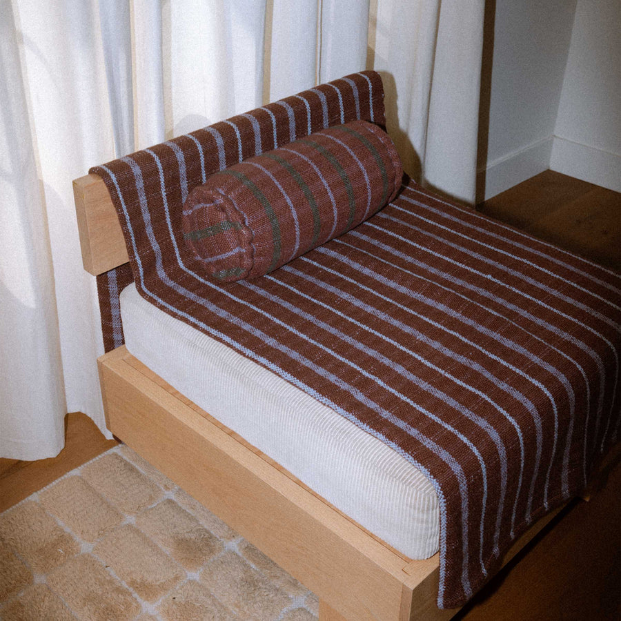 Brown and lavender bolster on top of a brown and lavender check blanket draped atop a chair.