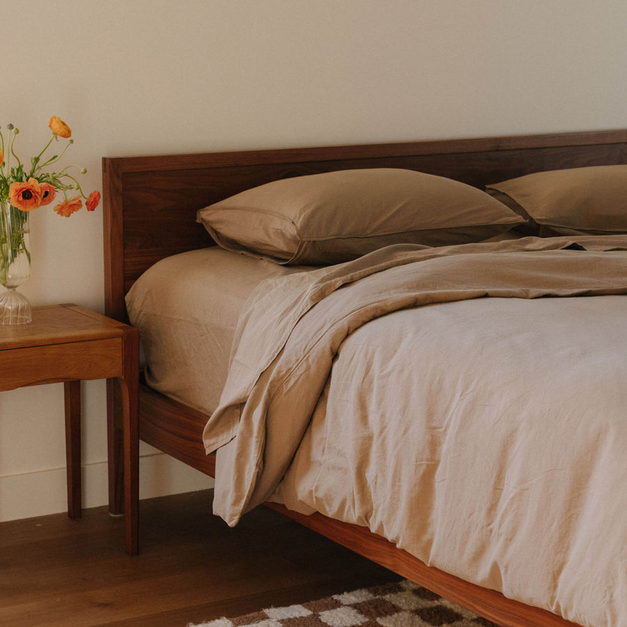 Bed in a bedroom setting with beige sheets. 