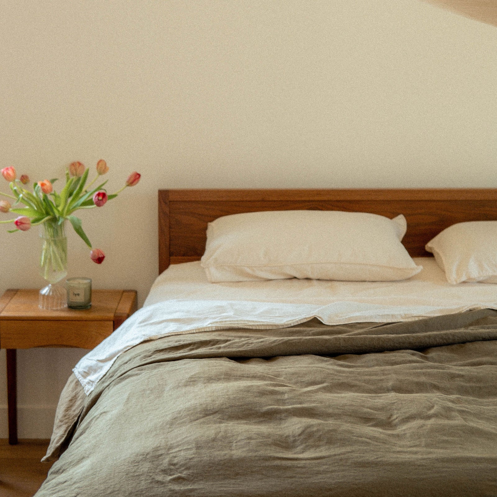 A bed dressed in oat pillows and sheets paired with a Fern duvet cover with a nightstand and flowers