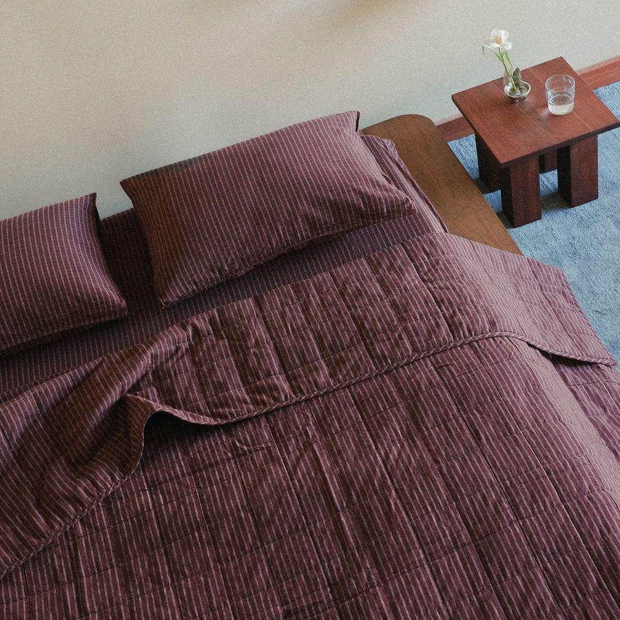 A birds-eye view of a brown striped quilt and pillows on a bed with a wooden side table in the background.