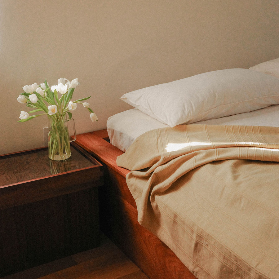 Bedroom with a bed dressed with white and beige sheets and a vase of flowers on a nightstand.