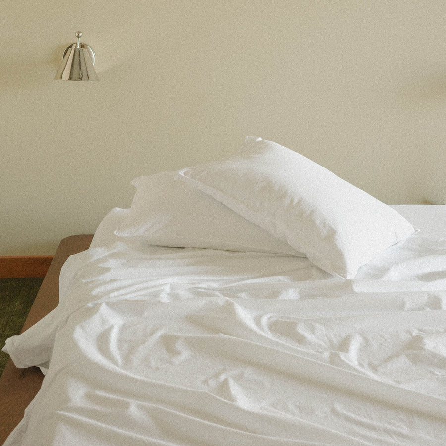 Bed with white sheets and pillows against a beige wall with a silver sconce.