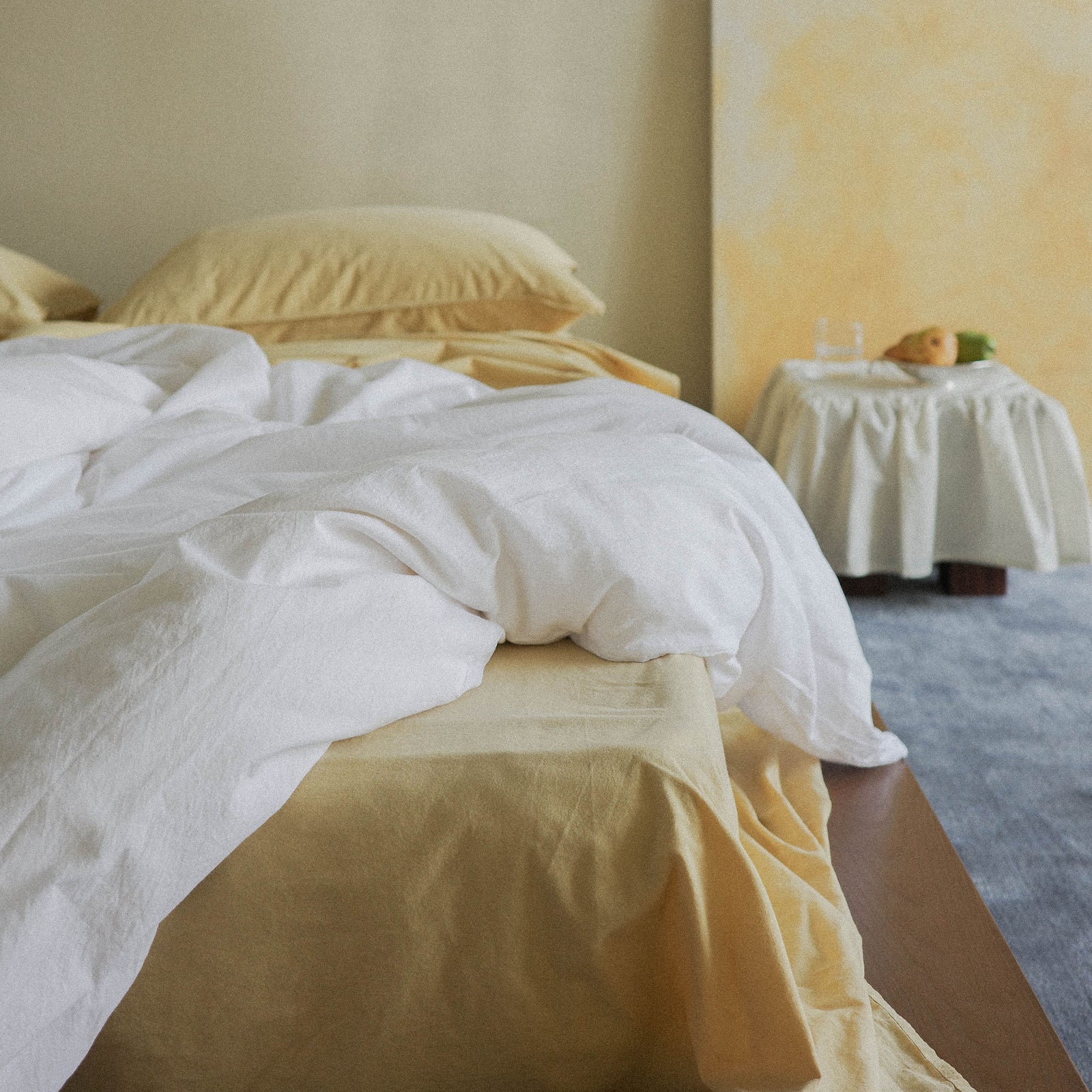 Bed with a white duvet cover over yellow sheets in a softly lit room with blurry background.