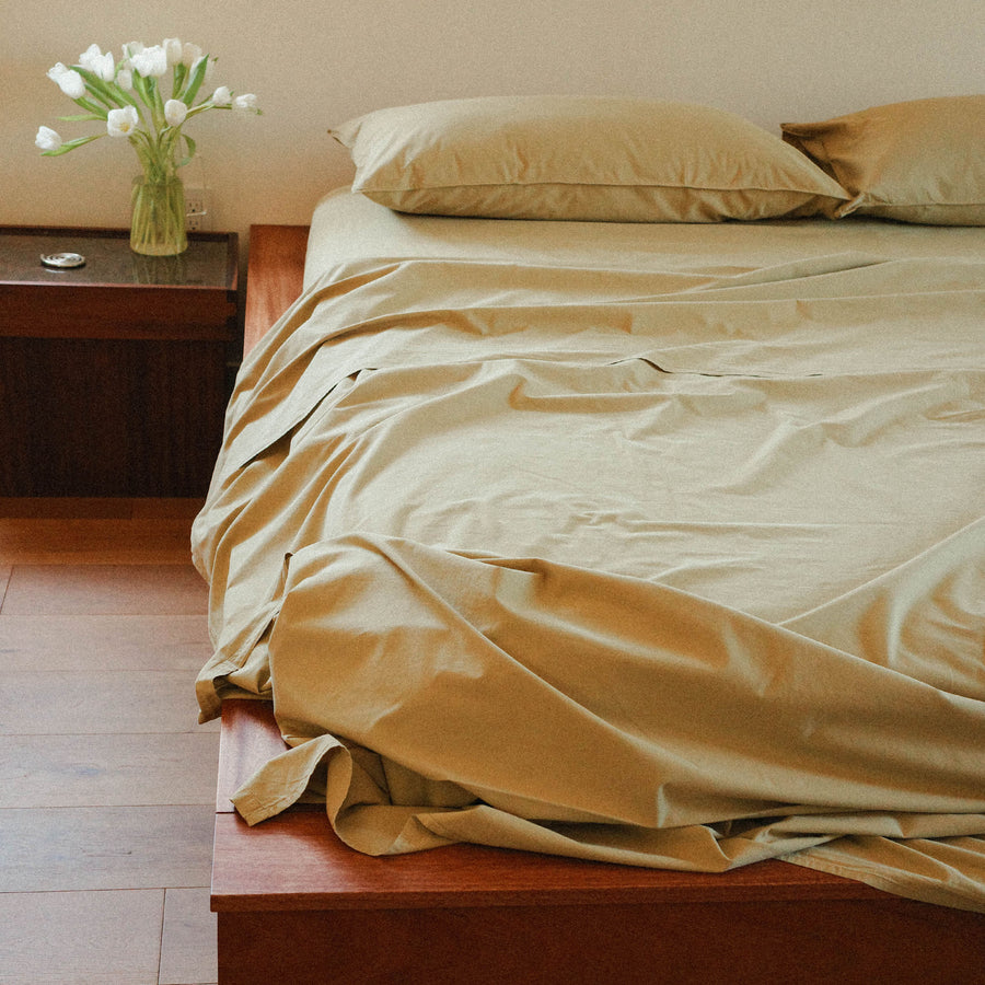 Bed with green sheets and pillows in a bedroom setting.