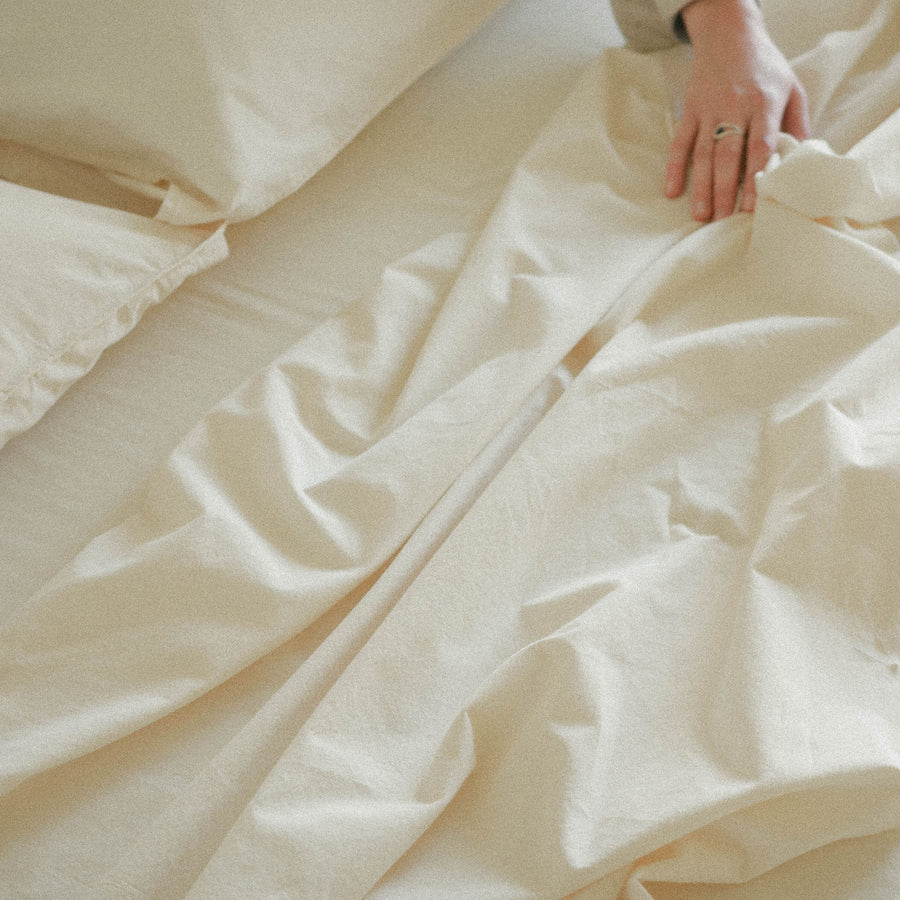 Close-up of cream bedding with a hand adjusting the top sheet
