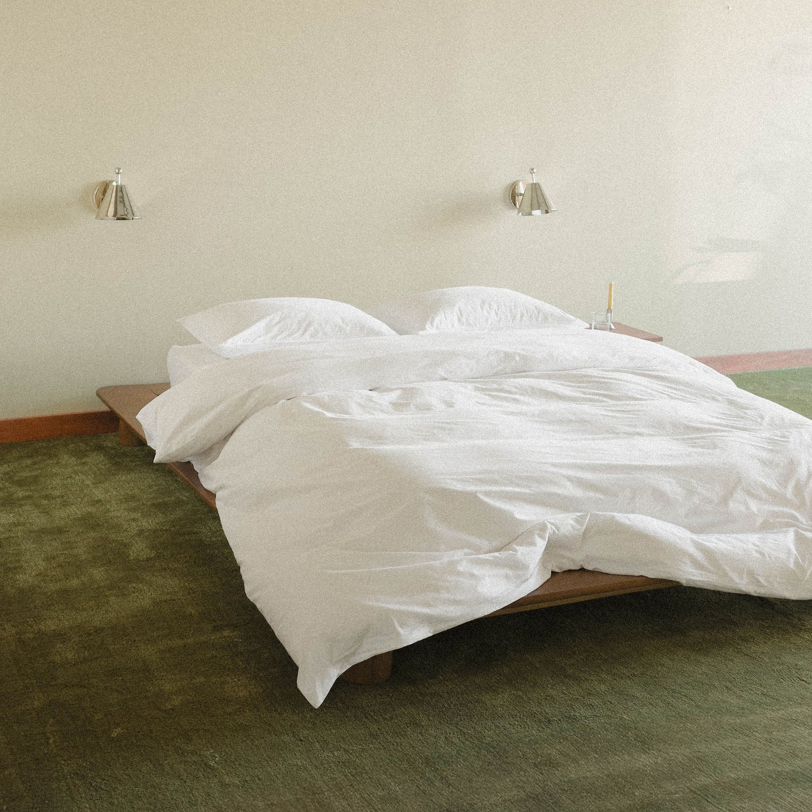Bed with white duvet cover and sheets in a room with green carpet and beige walls.