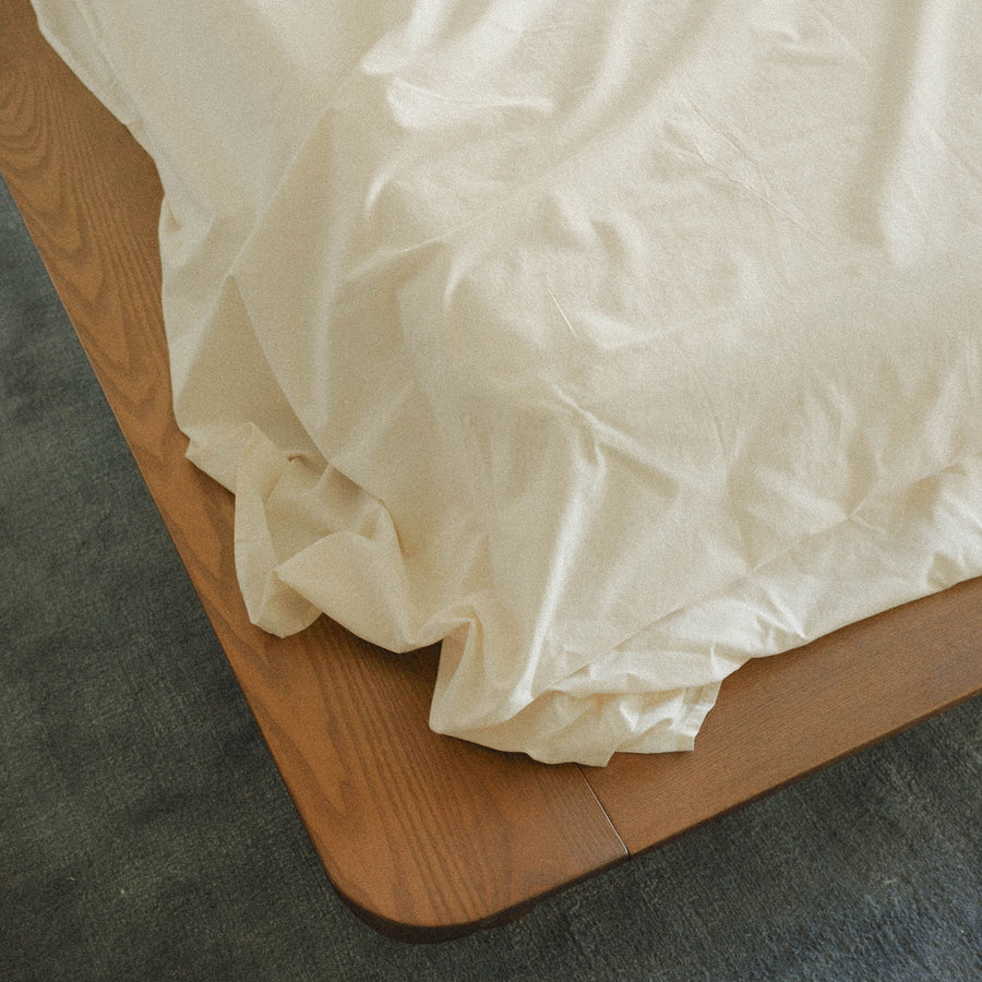 Cream bed sheets on a wooden bed frame with blue carpet.