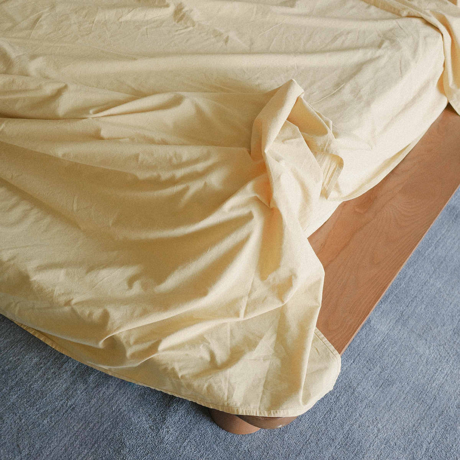 Yellow bed sheet draped over a wooden bed frame on a blue carpet.