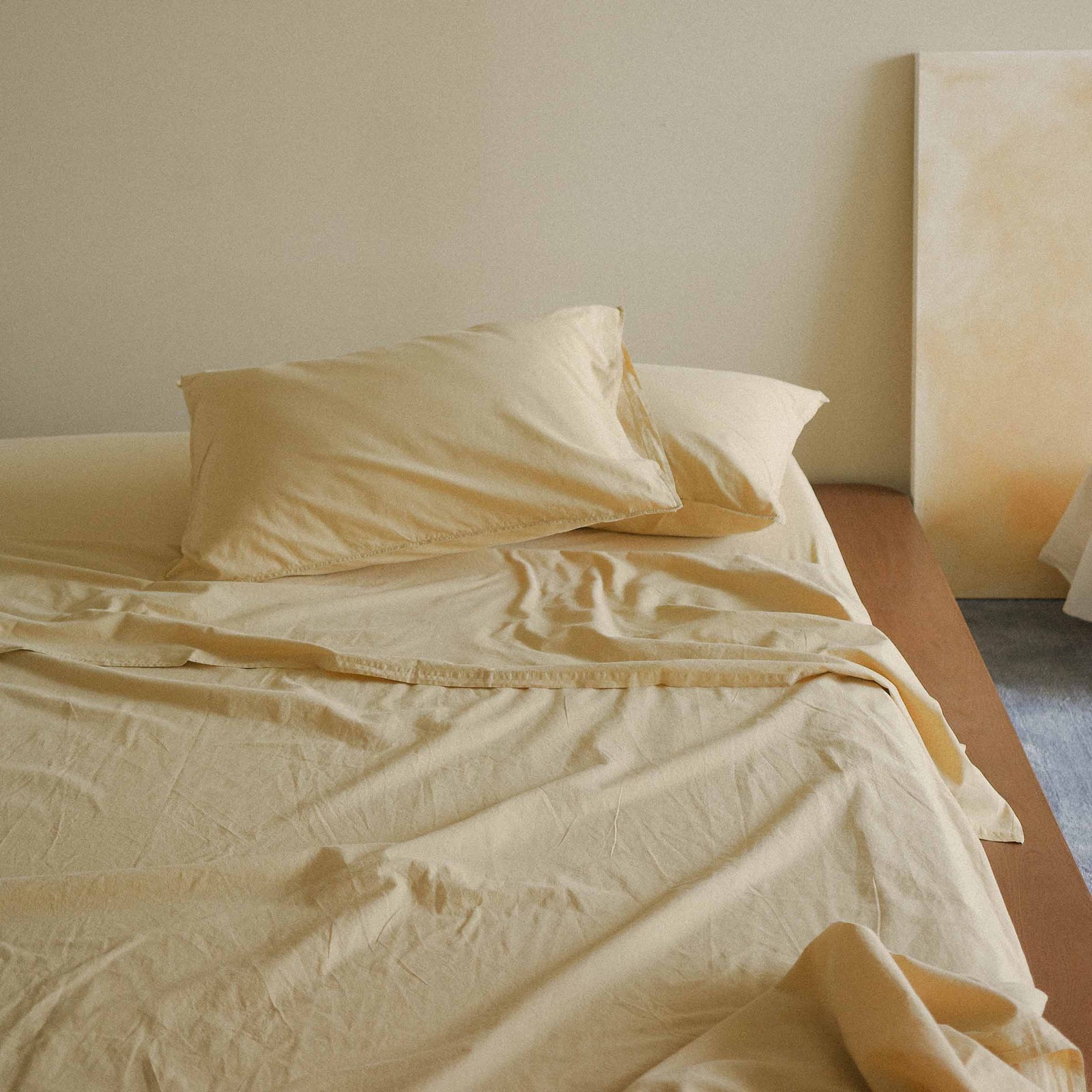 Yellow sheet set and pillows on a bed in a softly lit room.