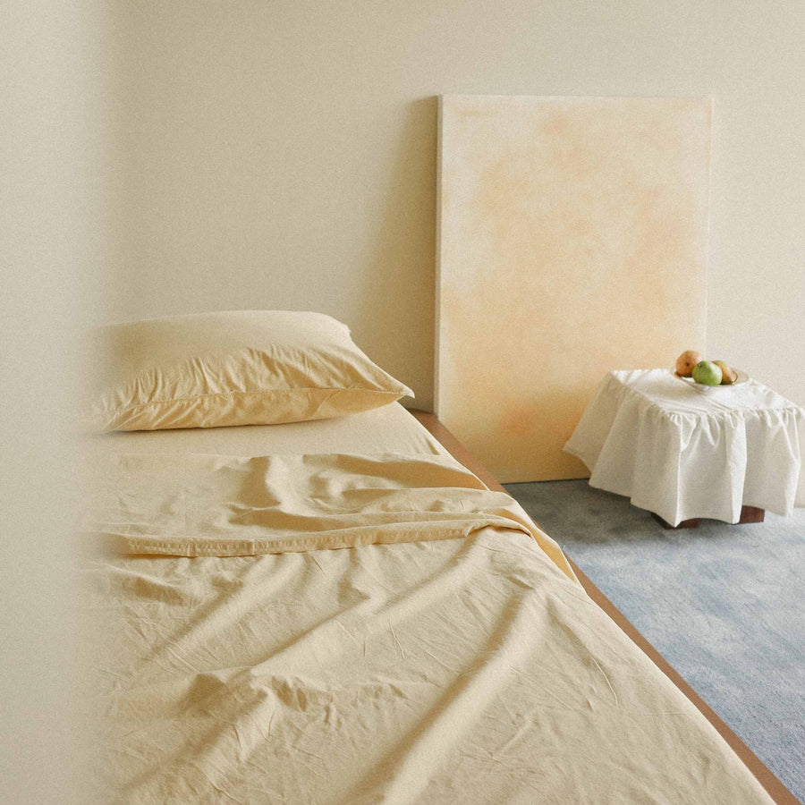 Yellow sheets on a bed with a neutral wall and table in the background