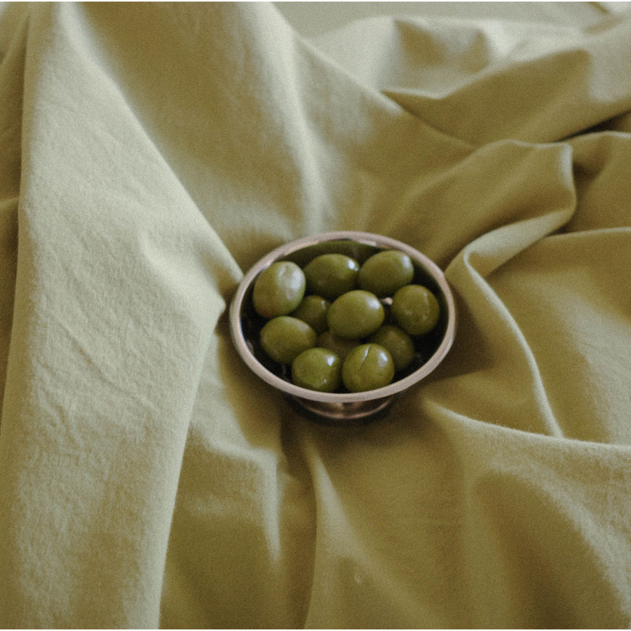 Bowl of green olives on a draped pale olive fabric background