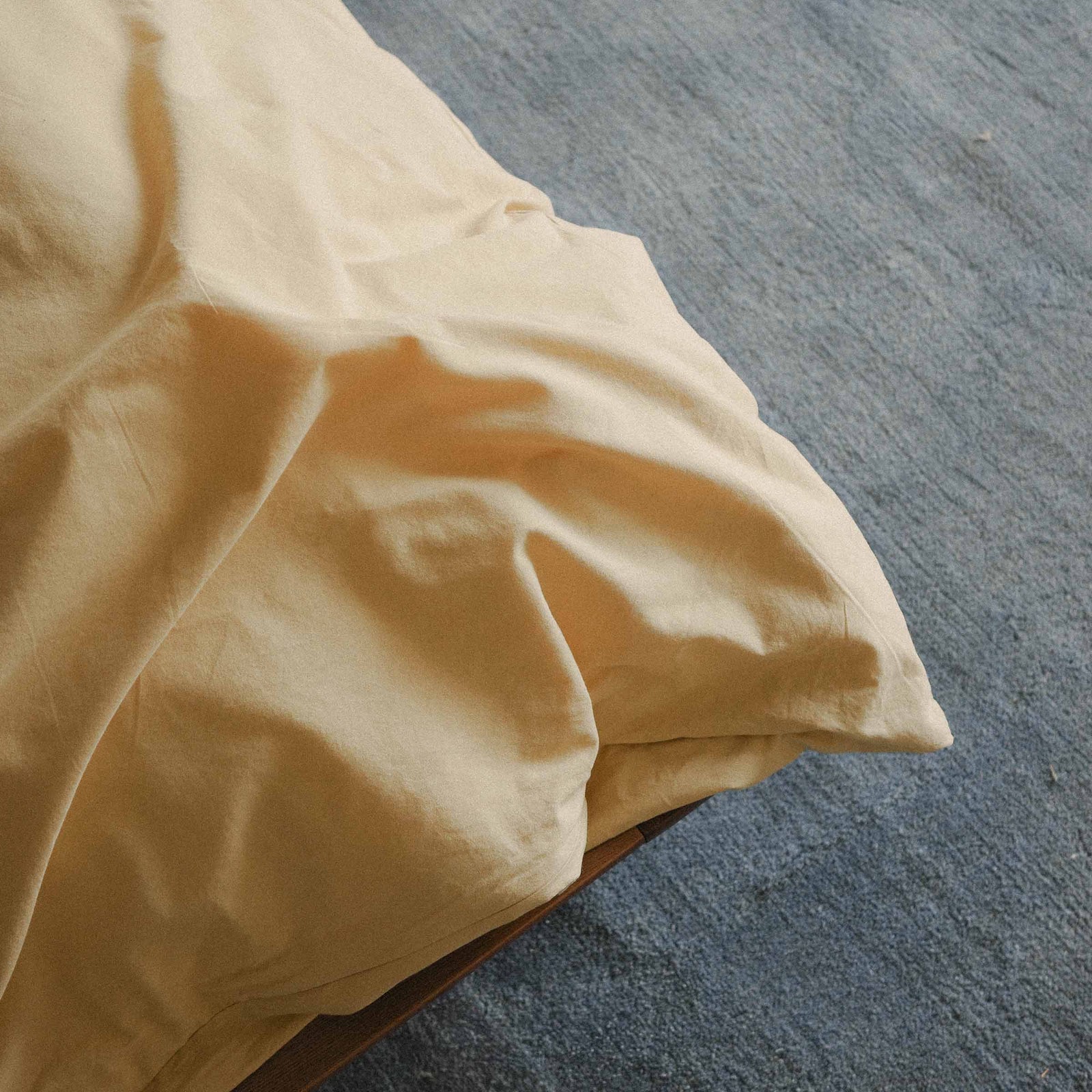 Yellow duvet cover on a bed with a blue carpeted floor.