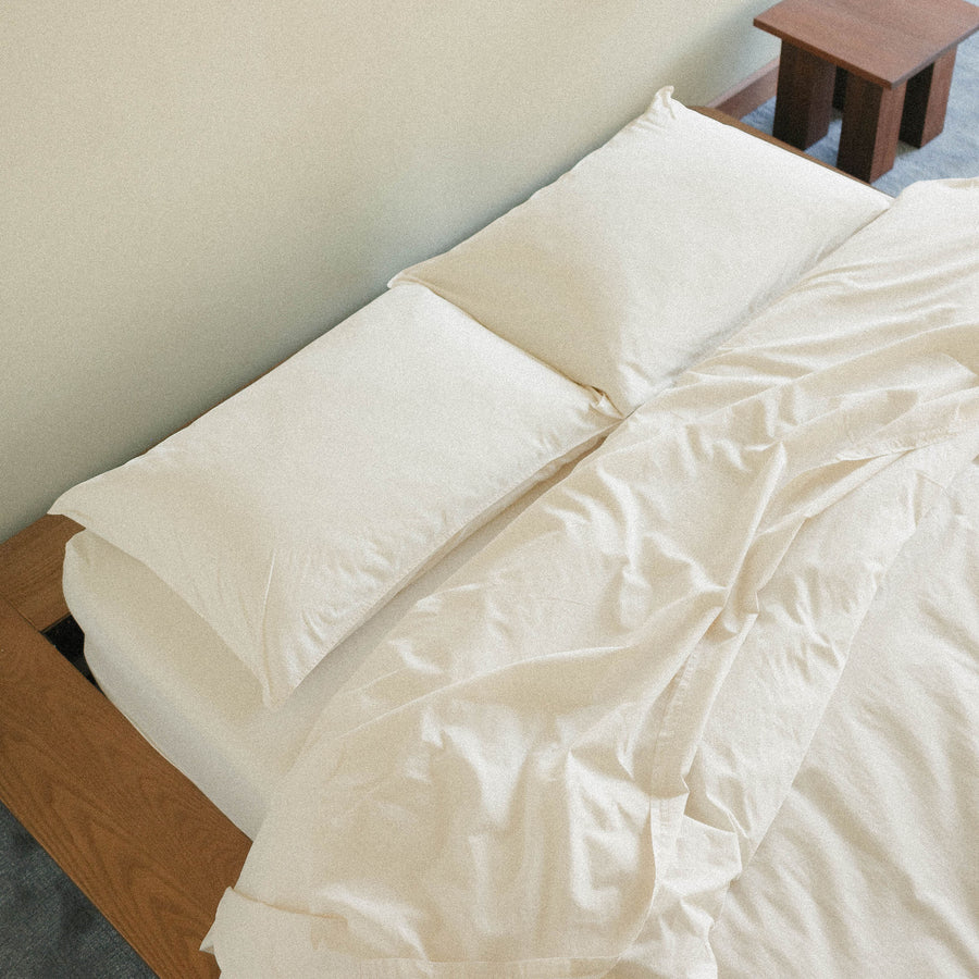 Neatly made bed with cream bedding and pillows in a bedroom setting.