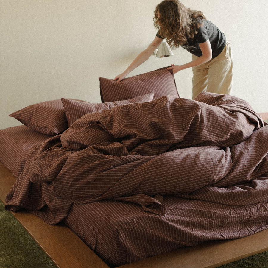 Woman arranging brown striped bedding on a bed including pillows in a bright bedroom
