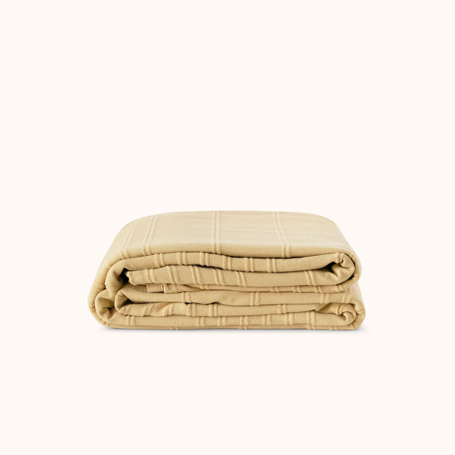 Folded beige / yellow blanket against a white background