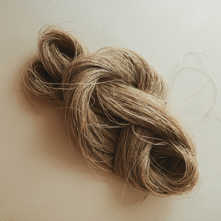 A bundle of hemp fiber in a twisted knot, resting on a neutral beige background.